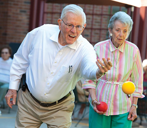 An elderly couple enjoying a game of bocce ball in the outdoors.