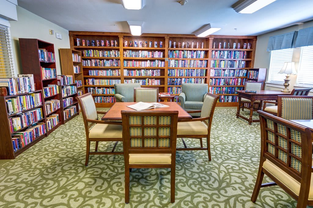 A cozy library with bookshelves, a reading table, and comfortable chairs.