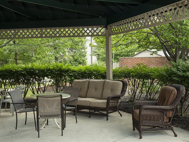 A cozy outdoor seating area under a gazebo, featuring comfortable chairs and a small table surrounded by greenery.