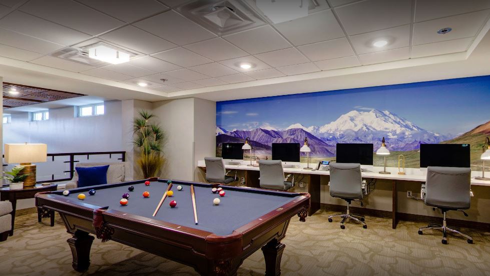 A modern game room featuring a pool table and computers, with a scenic mountain mural in the background.