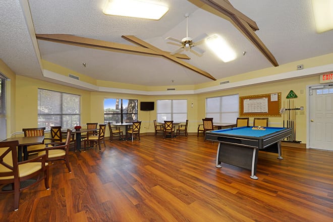 A spacious game room with a billiards table, hardwood floors, and ample seating.