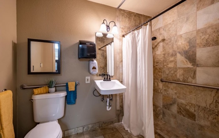 A clean and modern bathroom featuring a sink, toilet, mirror, and shower with a white curtain.