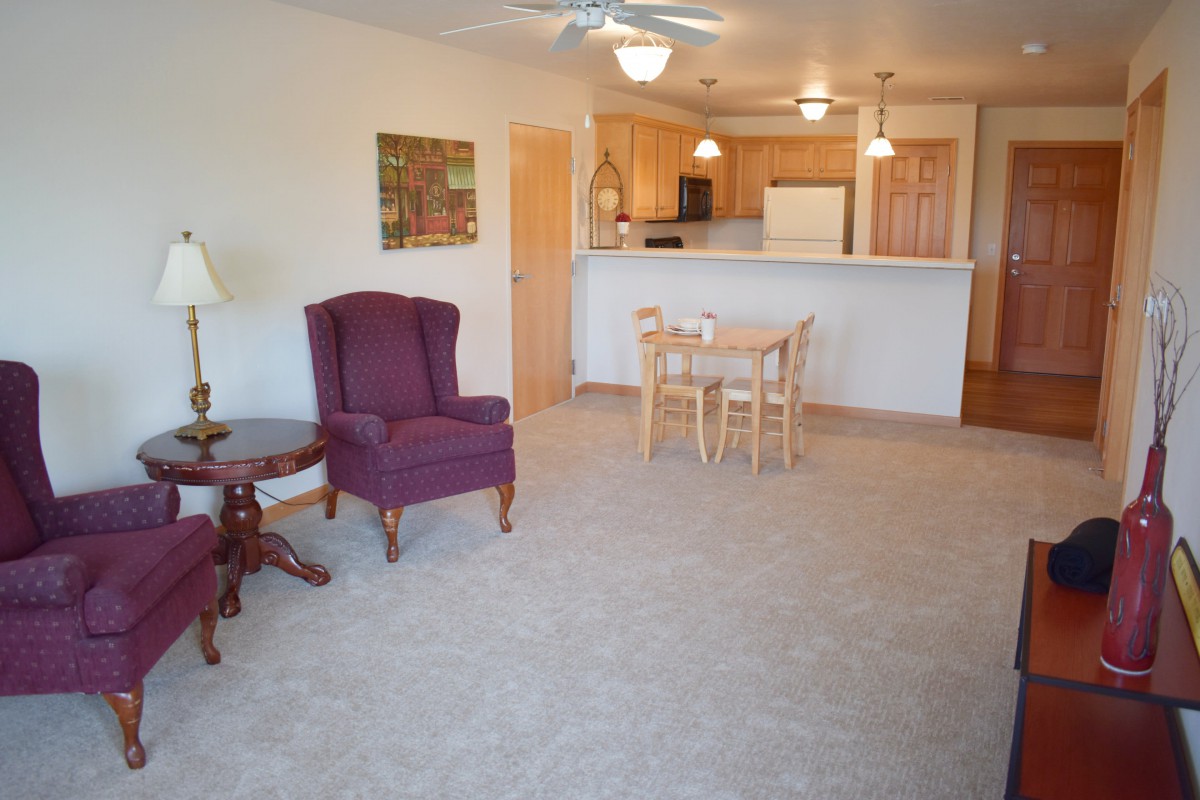 A cozy living room with an armchair, dining table, and an open view of the kitchen.