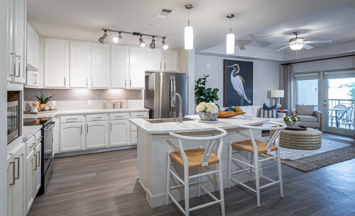 A modern kitchen featuring white cabinets, a central island with bar stools, pendant lighting, and stainless steel appliances.