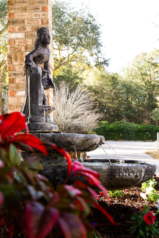 A serene garden fountain with a classical statue and vibrant foliage.