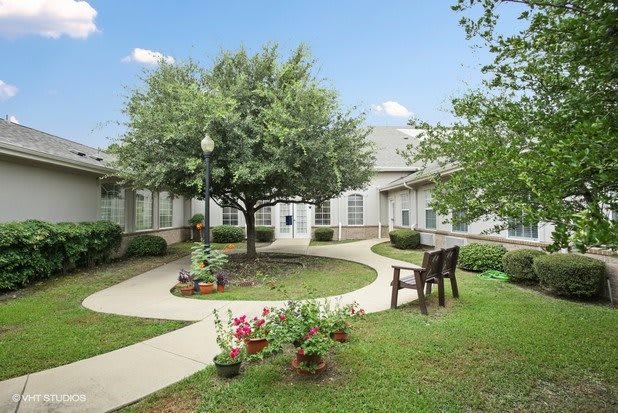 A peaceful garden area with pathways, benches, and trees surrounding a building.
