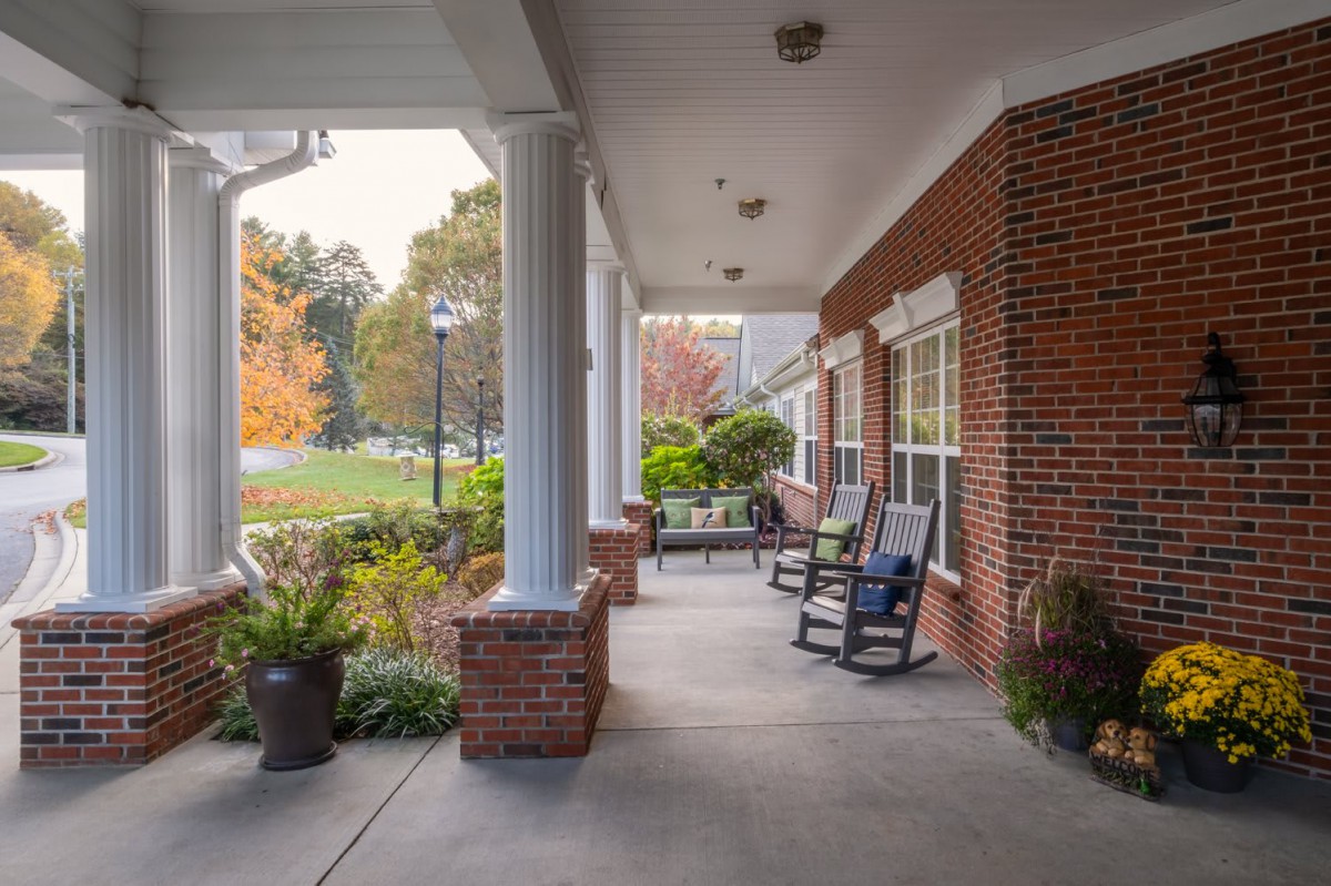 A cozy porch with rocking chairs and plants, attached to a brick building.