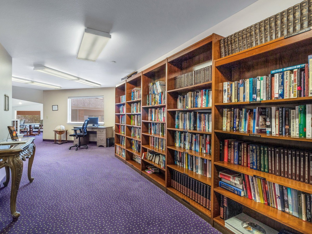 A cozy library room with bookshelves, a reading area, and a computer desk.