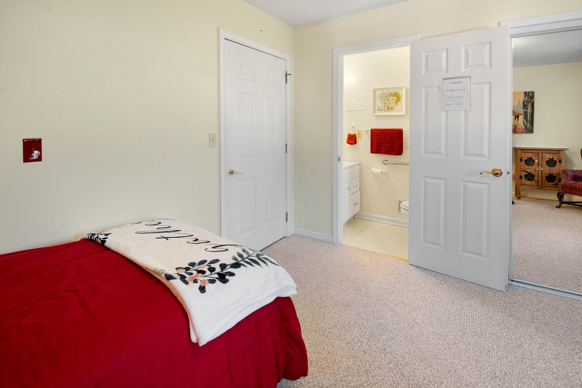 A cozy bedroom with a red blanket and access to an adjacent bathroom.