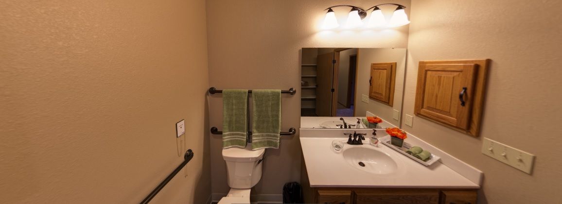 A well-lit bathroom featuring a toilet, sink with countertop, mirror, and neatly hung towels.