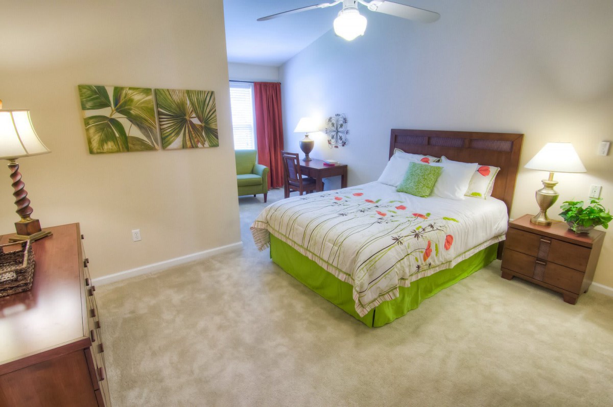 A cozy bedroom with a colorful bedspread, featuring a ceiling fan and decorative wall art.