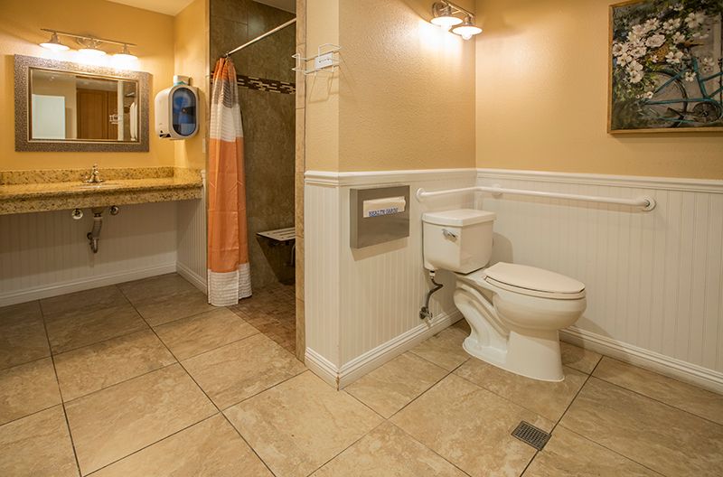 A clean and spacious bathroom with a toilet, sink, mirror, and shower area.
