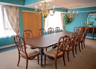 An elegant dining room featuring a large wooden table surrounded by matching chairs, with chandeliers and draped curtains adding a touch of sophistication.