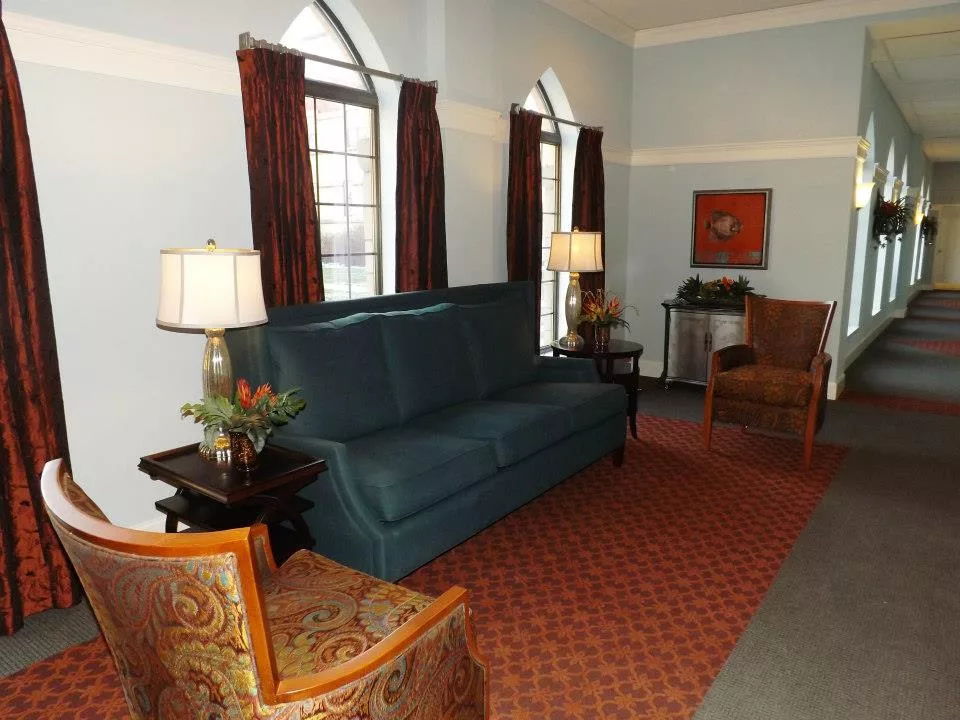 A cozy living room featuring a blue sofa, armchairs, and tall arched windows with red curtains.