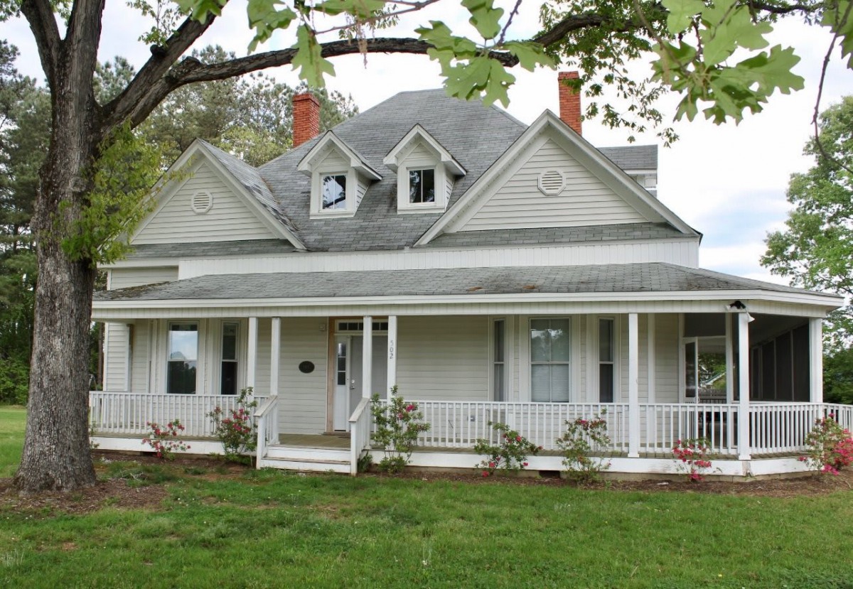A charming Victorian-style house with a spacious front porch and a well-maintained lawn.