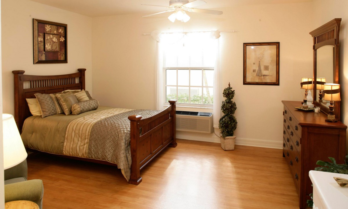 A cozy bedroom with wooden flooring, featuring a bed and a window letting in natural light.