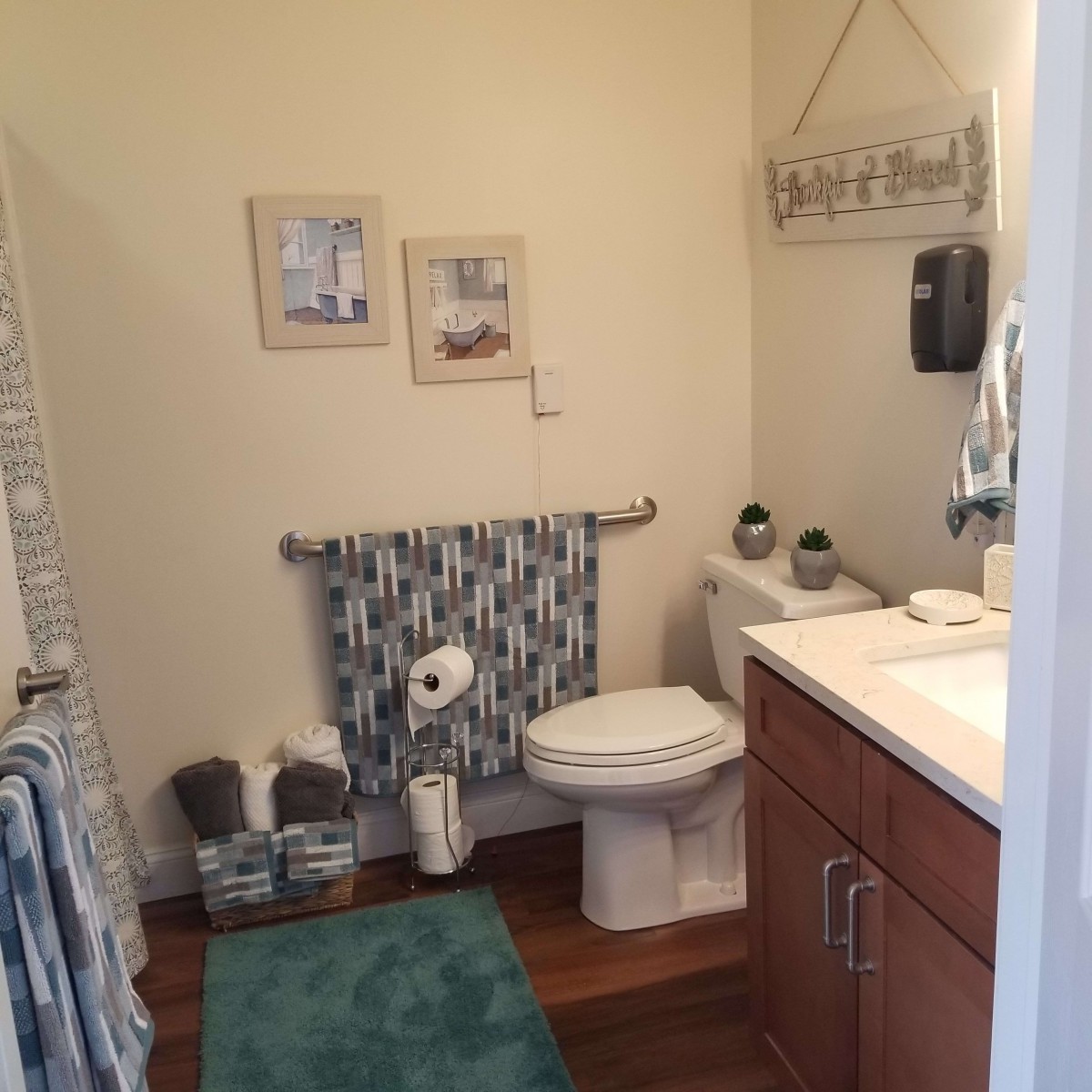 A neatly arranged bathroom with decorative elements, featuring a toilet, towels, wall art, and a rug.