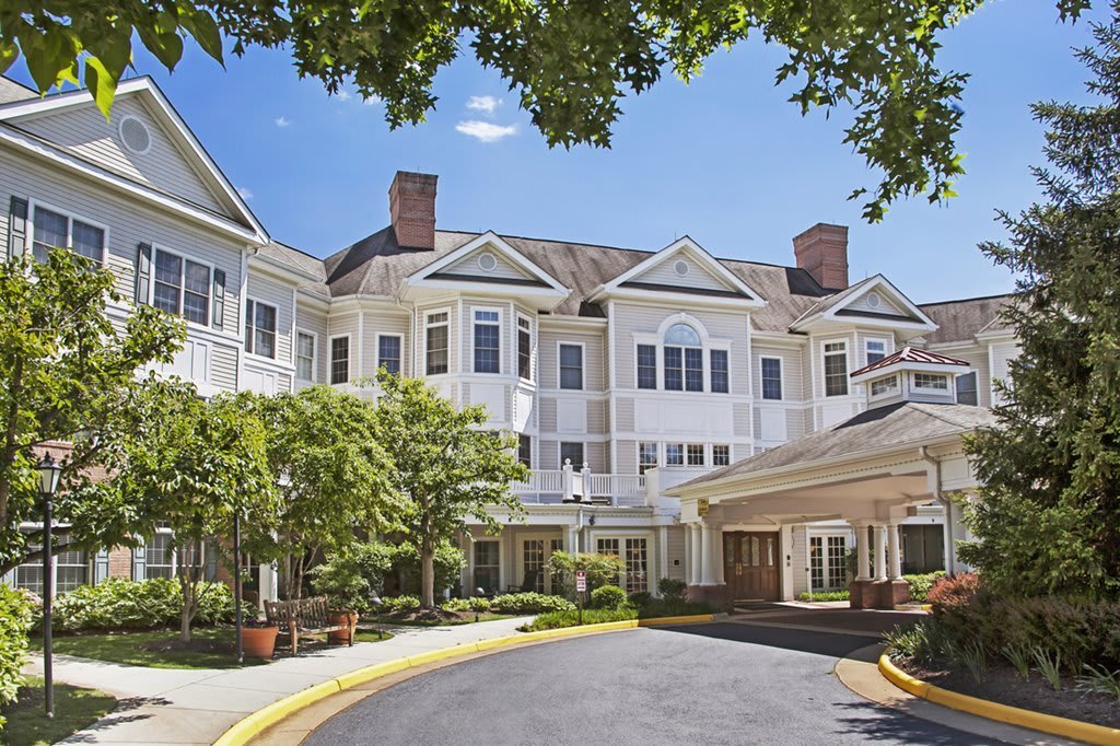 A large residential building with an entrance surrounded by trees under a clear blue sky.