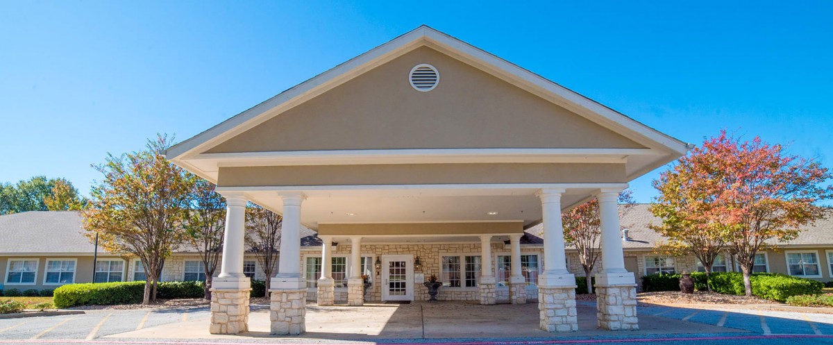 The image shows the front entrance of a building with a covered walkway supported by columns.