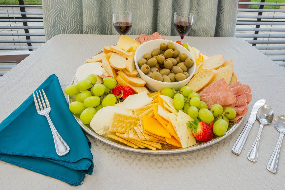 A charcuterie board featuring a variety of cheeses, meats, crackers, olives, and grapes, accompanied by glasses of wine.
