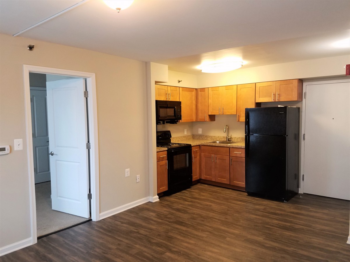 A modern apartment kitchen with wooden cabinets and black appliances.