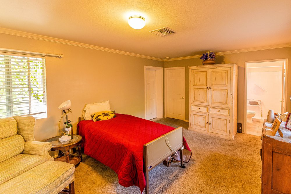 Cozy bedroom with a single bed covered in a red bedspread, featuring a wardrobe and warm lighting.