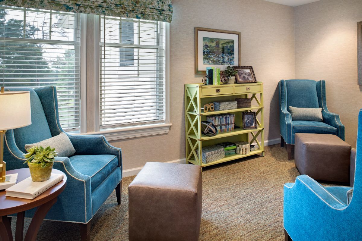 A cozy living room with colorful chairs, a bookshelf, and a window bringing in natural light.