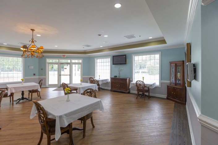 A spacious and bright dining room with neatly arranged tables and chairs, featuring large windows and a wooden floor.