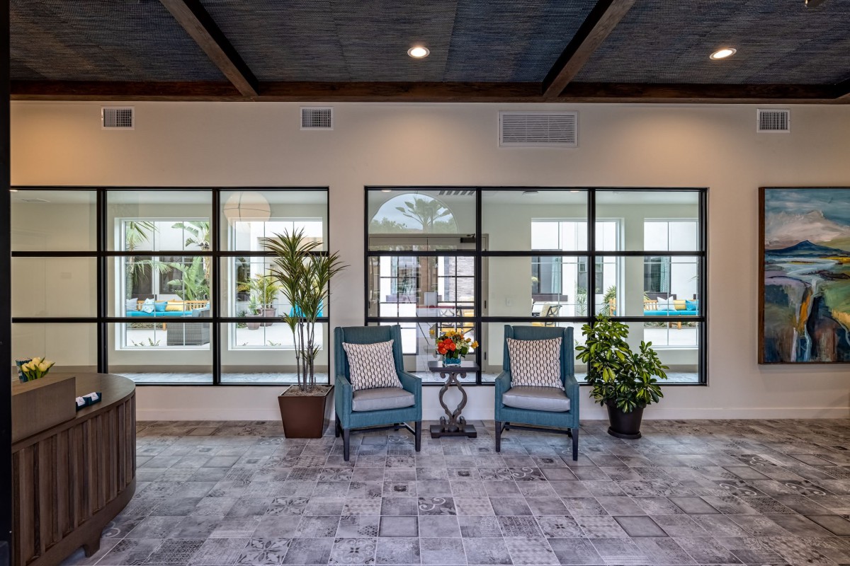A stylish indoor seating area with two chairs and decorative plants in front of large windows.