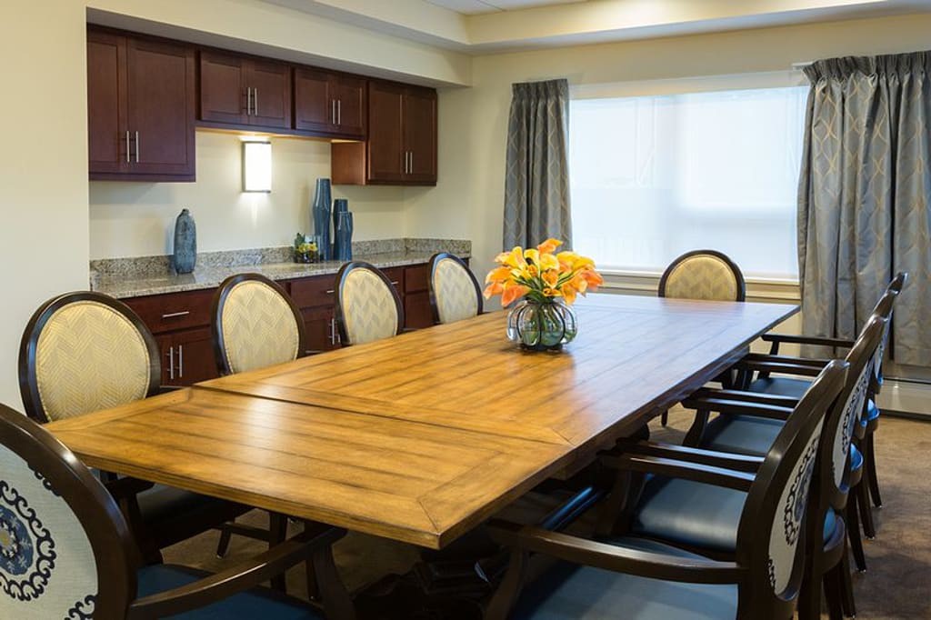 A well-lit conference room with a large wooden meeting table and elegant chairs, featuring decorative vases and a bouquet of flowers.