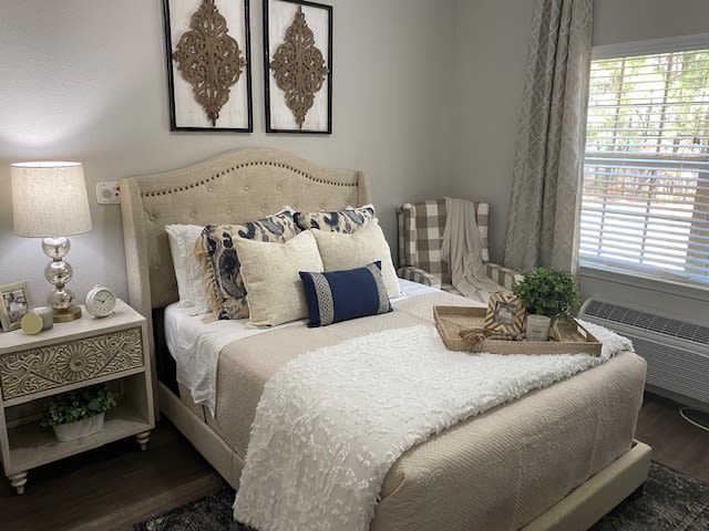 A cozy and elegantly decorated bedroom with a neatly made bed featuring multiple pillows, artwork above the headboard, and a tray placed on the bed.