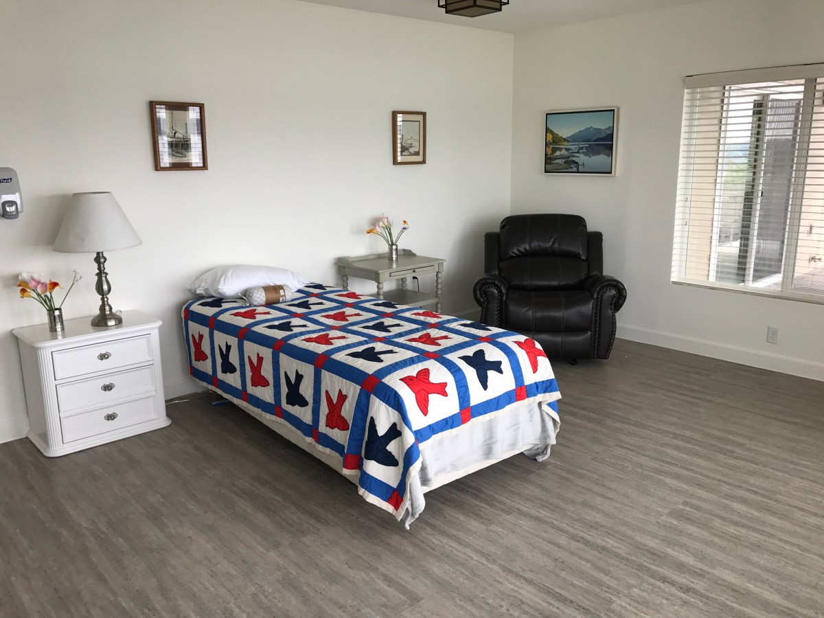 A minimalist bedroom featuring a single bed with a colorful quilt, alongside a black recliner chair.