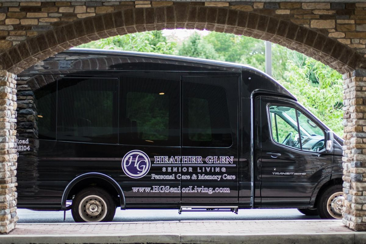 A black van under a bridge with signage for senior care and luxury transportation services.