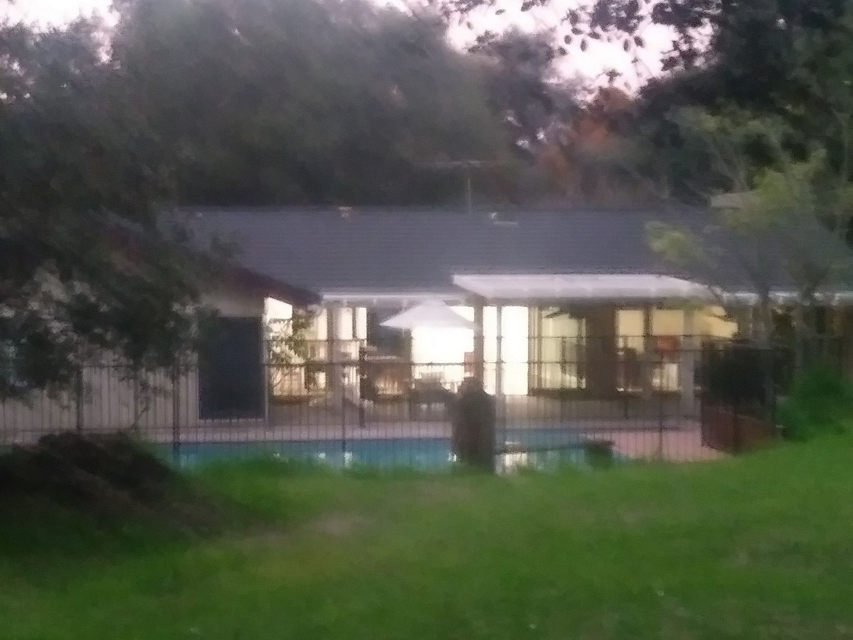 A cozy house with illuminated windows and a pool in the backyard during the evening.