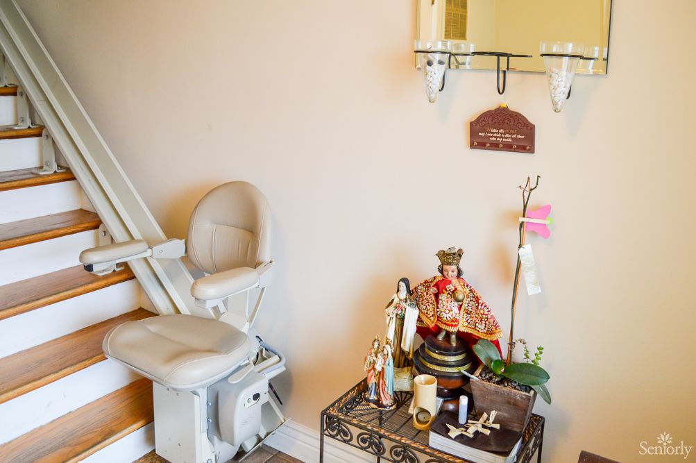 A cozy home corner featuring a stair lift and a small religious altar adorned with statues and candles.