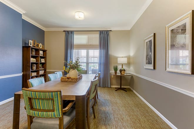 A well-decorated dining room featuring a wooden table, chairs with striped upholstery, and neutral-colored walls complemented by blue curtains.