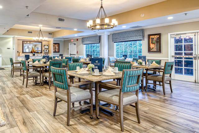 A beautifully decorated dining area with multiple tables and chairs, elegant chandeliers, and large windows offering a pleasant ambiance.