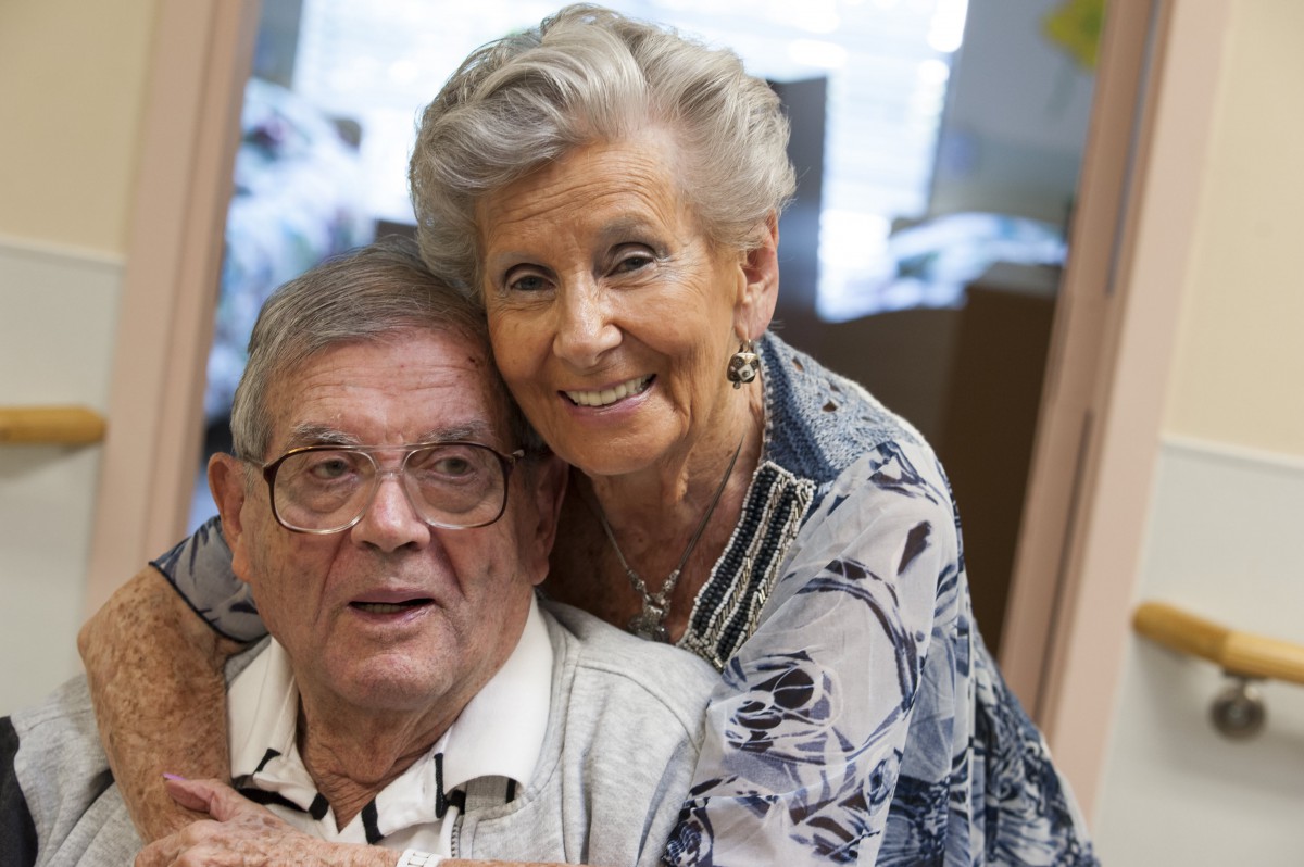 An elderly couple smiling warmly indoors, showcasing togetherness and happiness.