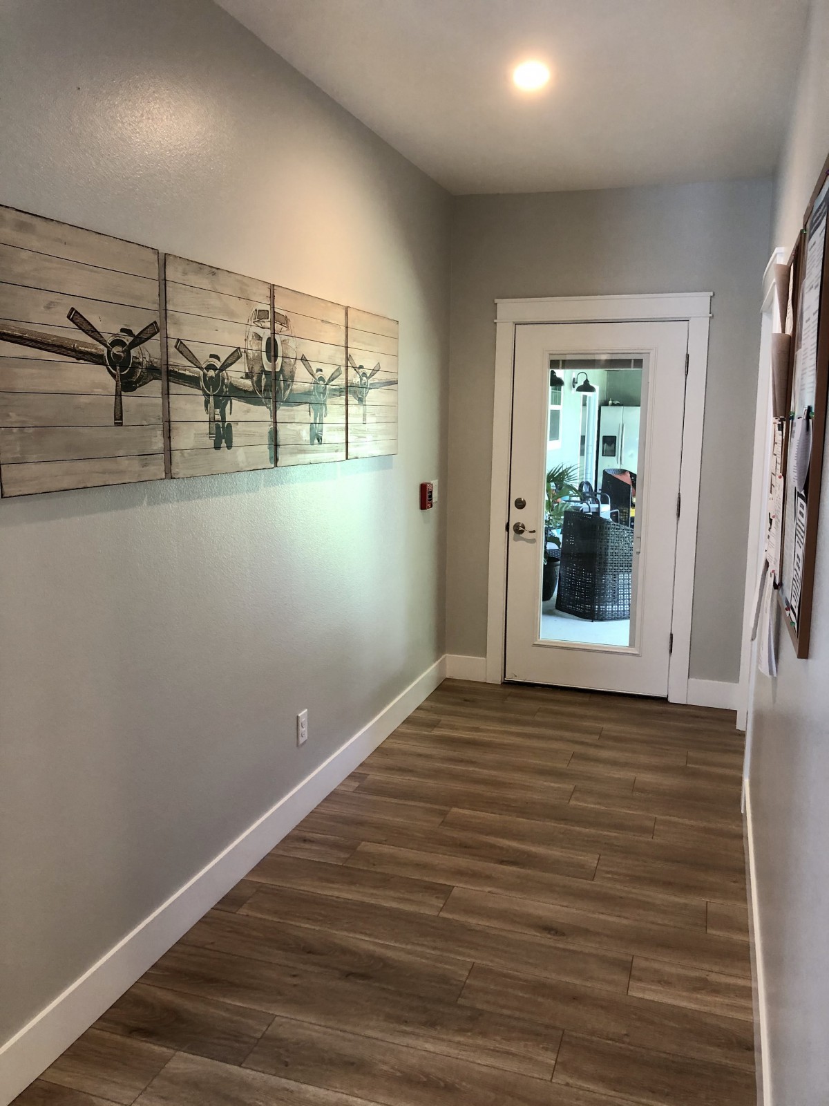 A modern hallway with wooden flooring and wall art, leading to a glass door.