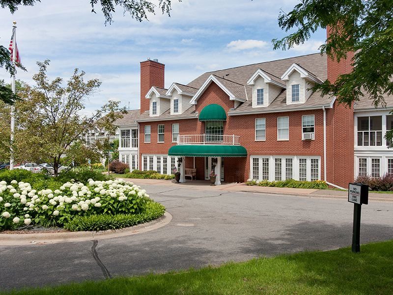 A charming brick hotel with a landscaped driveway and lush greenery.
