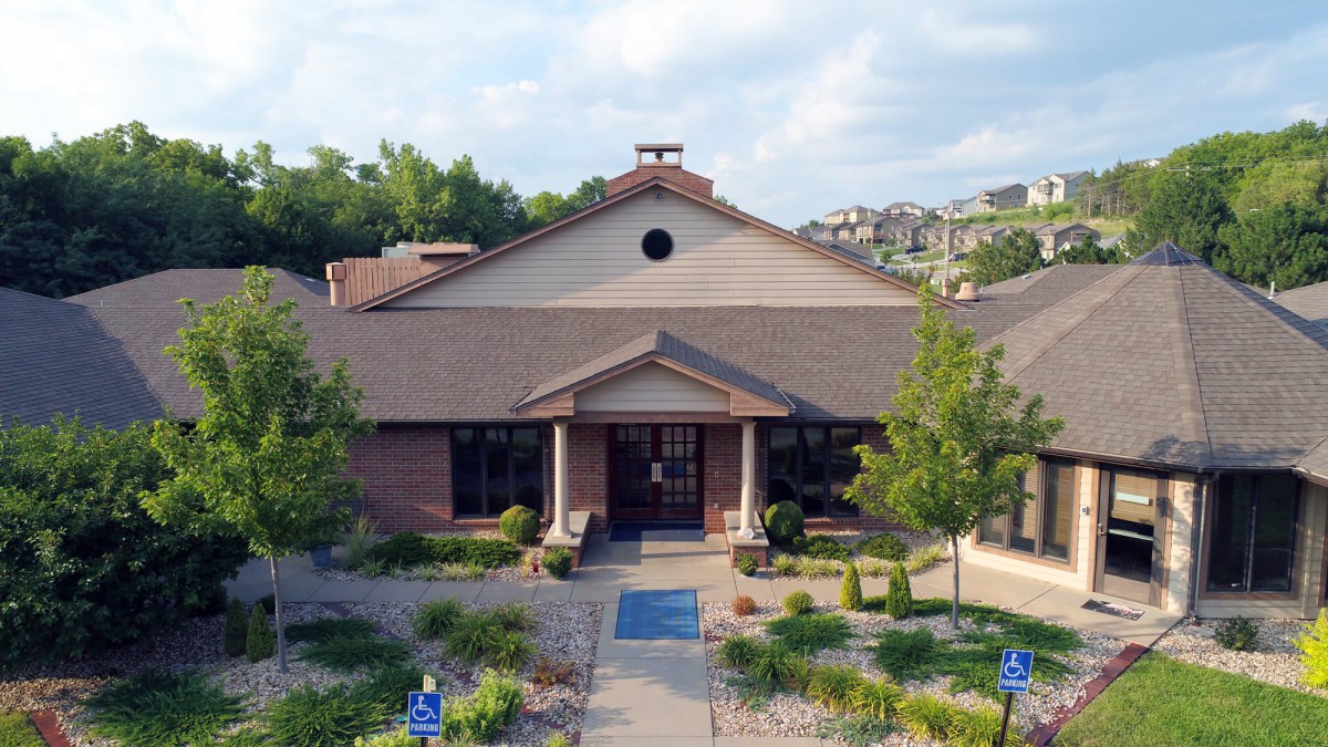 A front view of a building with a pathway leading to the entrance, surrounded by greenery.