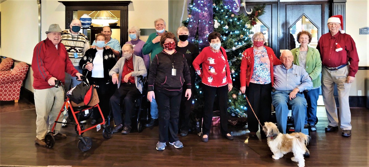 A group of people standing in front of a decorated Christmas tree, wearing festive clothing and masks.