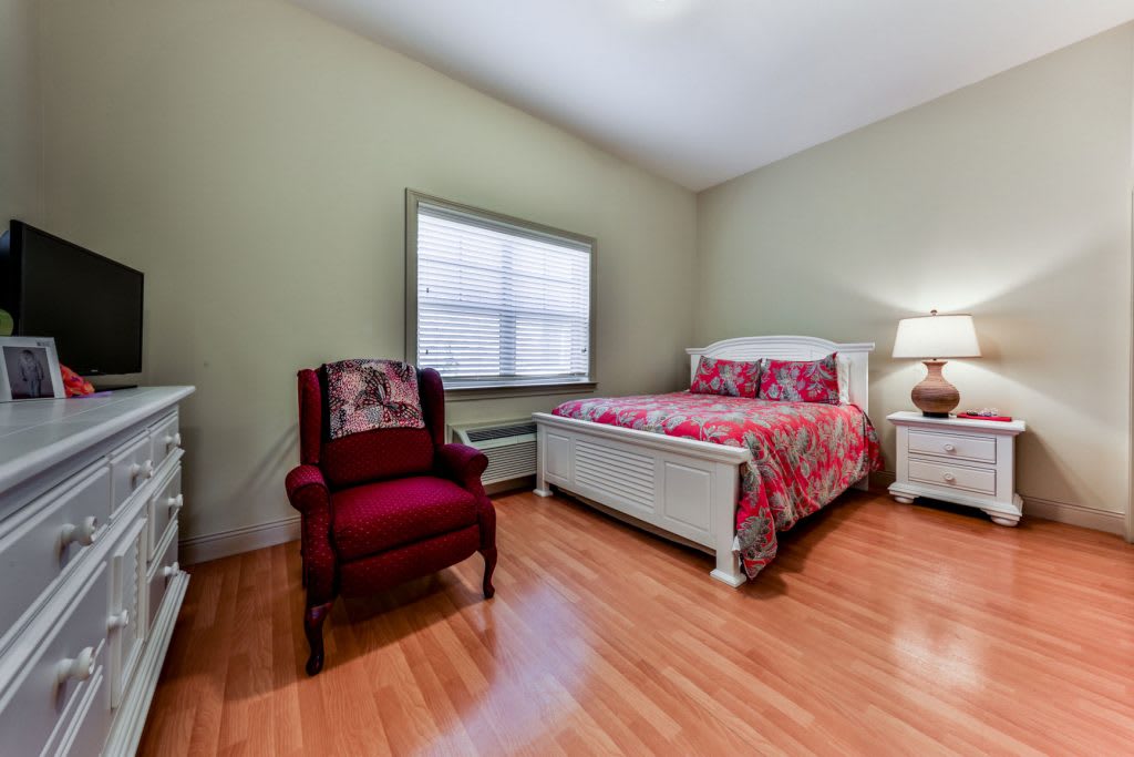 A cozy bedroom with a bed, chair, and lamp on wooden flooring.