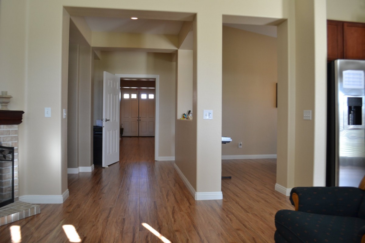 A view of a hallway with wooden flooring and an open door leading to another room.