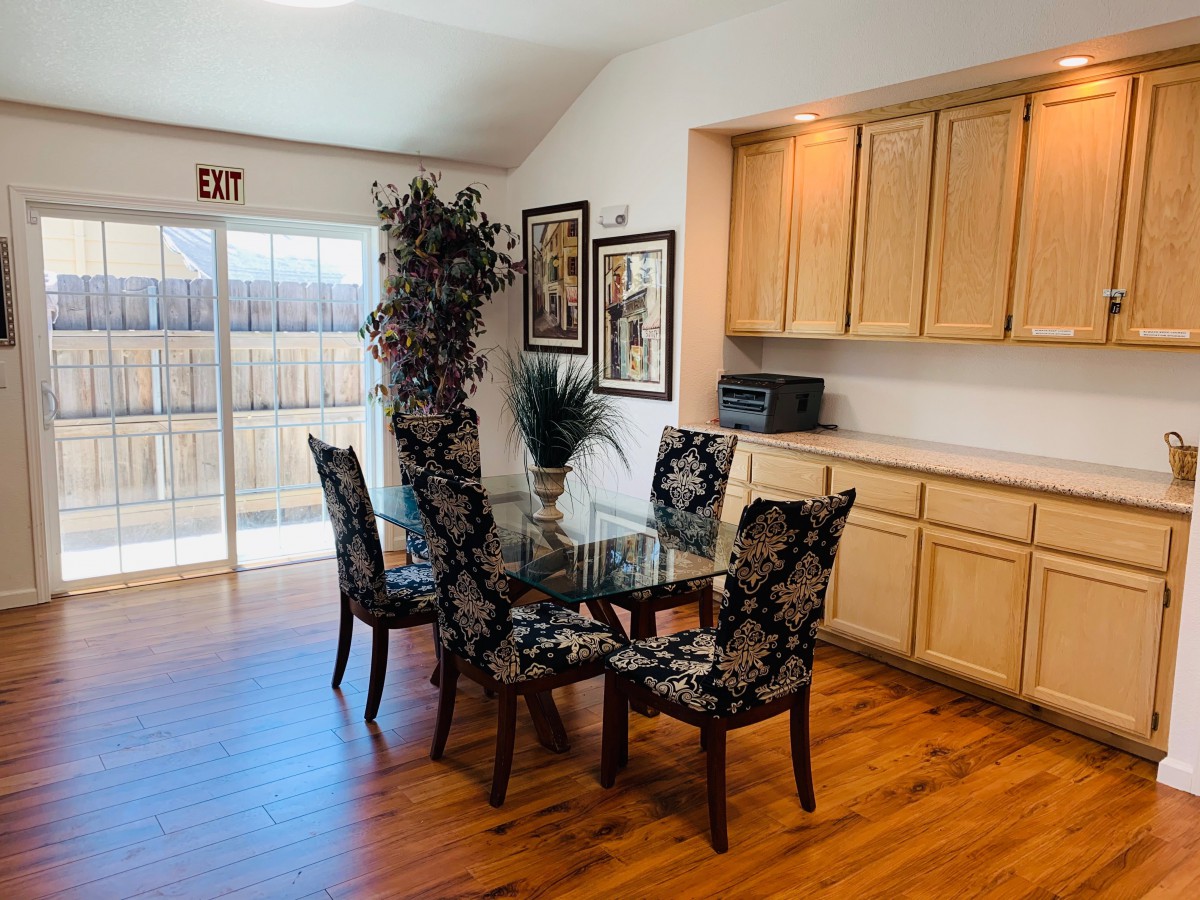 A cozy dining area featuring a glass table with four upholstered chairs, surrounded by warm wood flooring and decorative wall art.