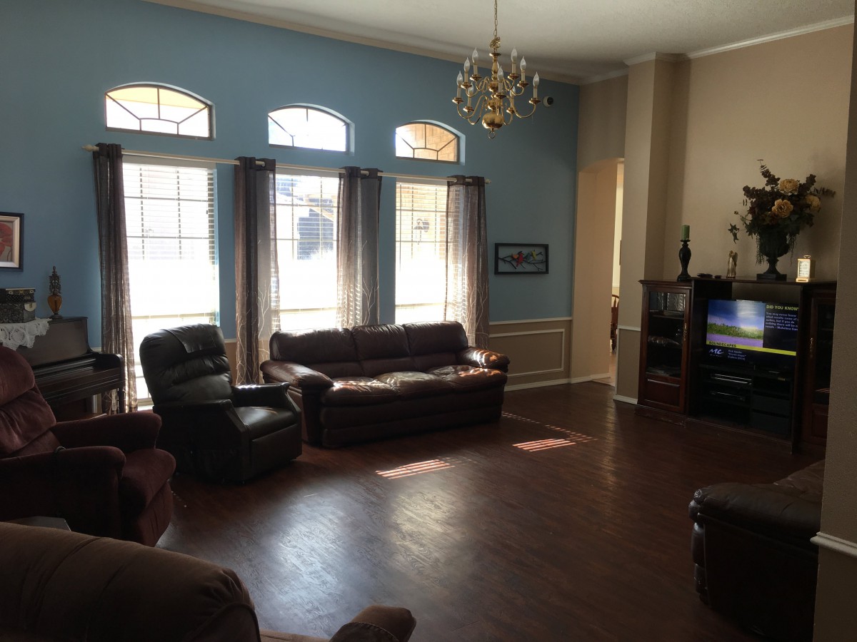 A spacious living room with large windows, leather sofas, a chandelier, and wooden flooring.