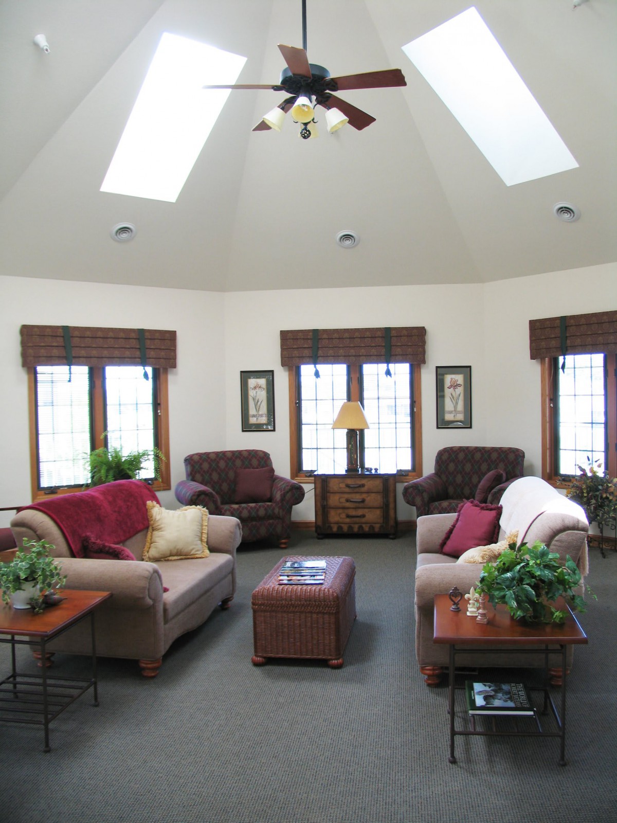 A cozy living room with multiple sofas, natural light from skylights and windows, and decorative plants.