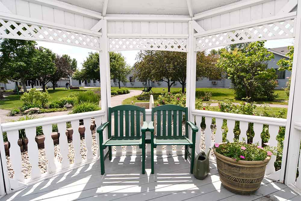A peaceful view from inside a white gazebo with green benches overlooking a garden path.