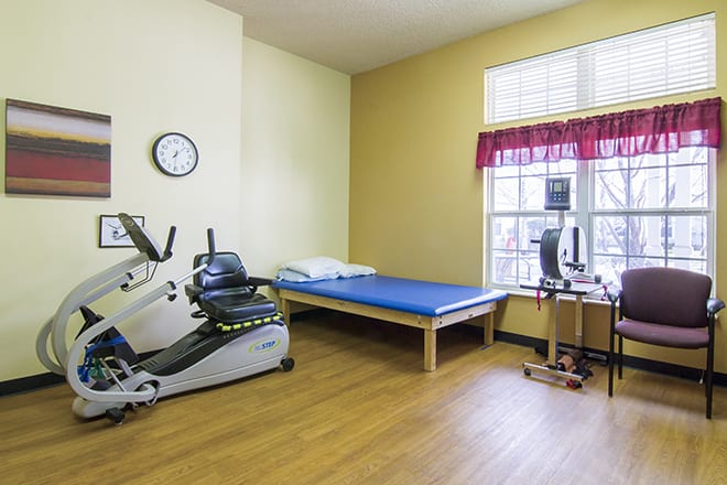 A rehabilitation room featuring a recumbent bike and an exercise mat, designed for physical therapy and fitness exercises.