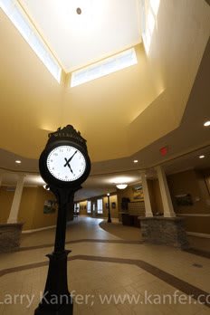 A large clock stands in the center of a spacious lobby with high ceilings and warm lighting.